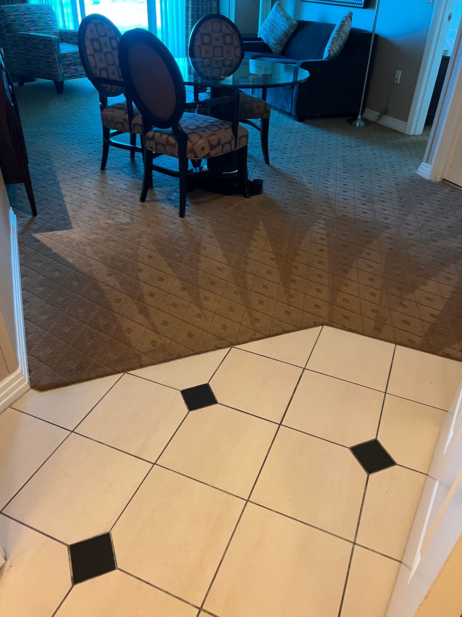 Tiled entryway leading to a room with patterned carpet, chairs, and a table.
