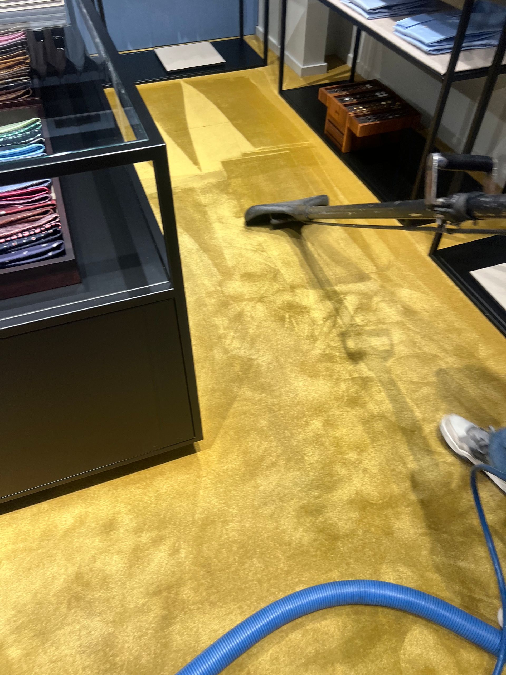 Yellow carpet being vacuumed in a retail store. A worker and equipment are visible.