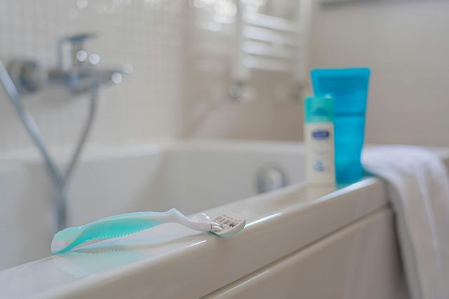 A razor and toiletries on the edge of a white bathtub in a bathroom.