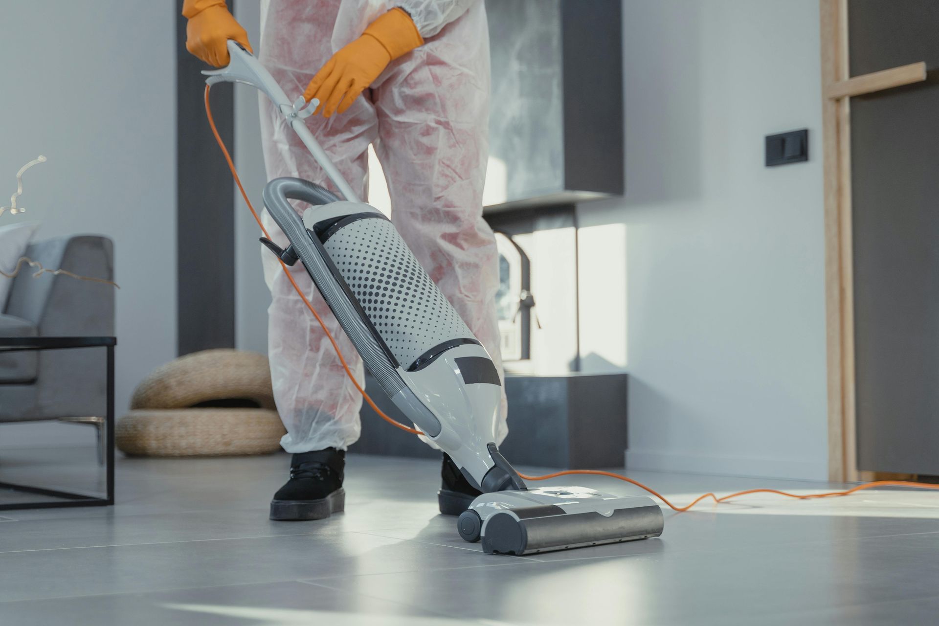 Person in hazmat suit vacuuming a floor in a modern living room.