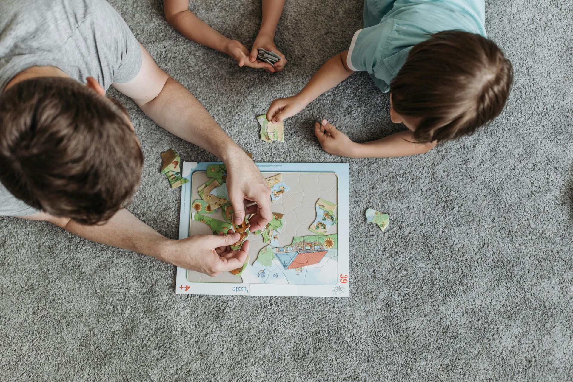 Person and two children assembling a world map puzzle on a gray carpet.