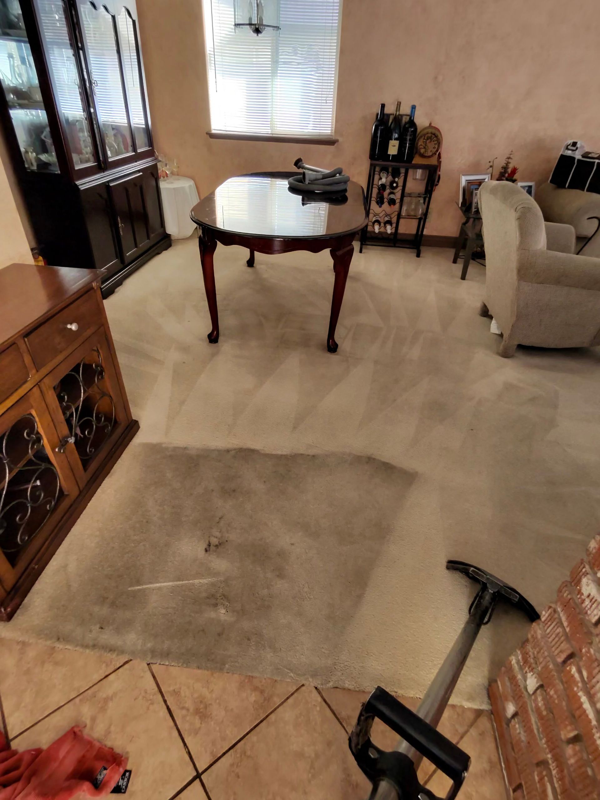 Carpeted room with furniture: dining table, cabinets, couch, and a carpet cleaner in use.
