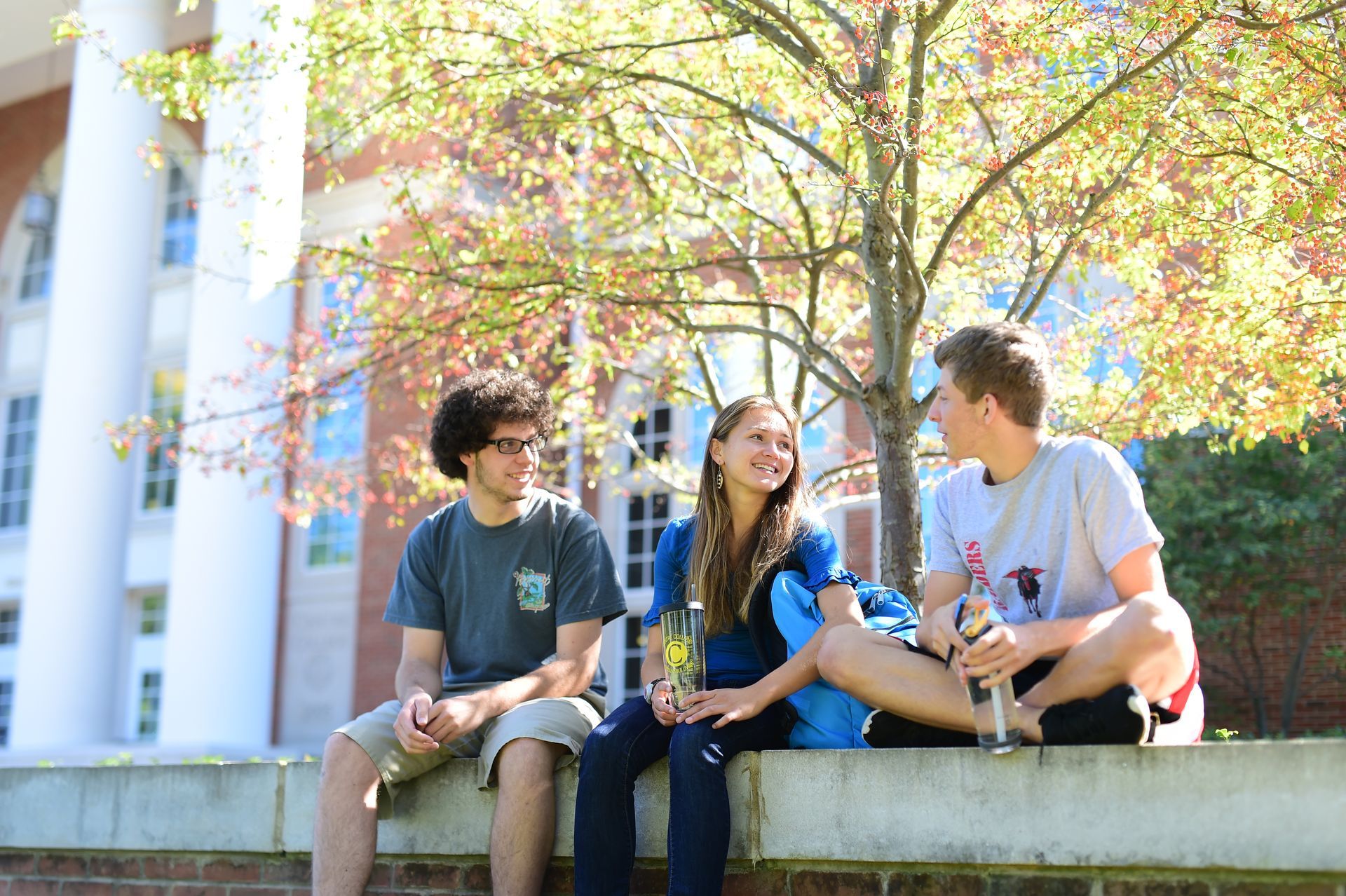 Three people are sitting on a wall talking to each other.