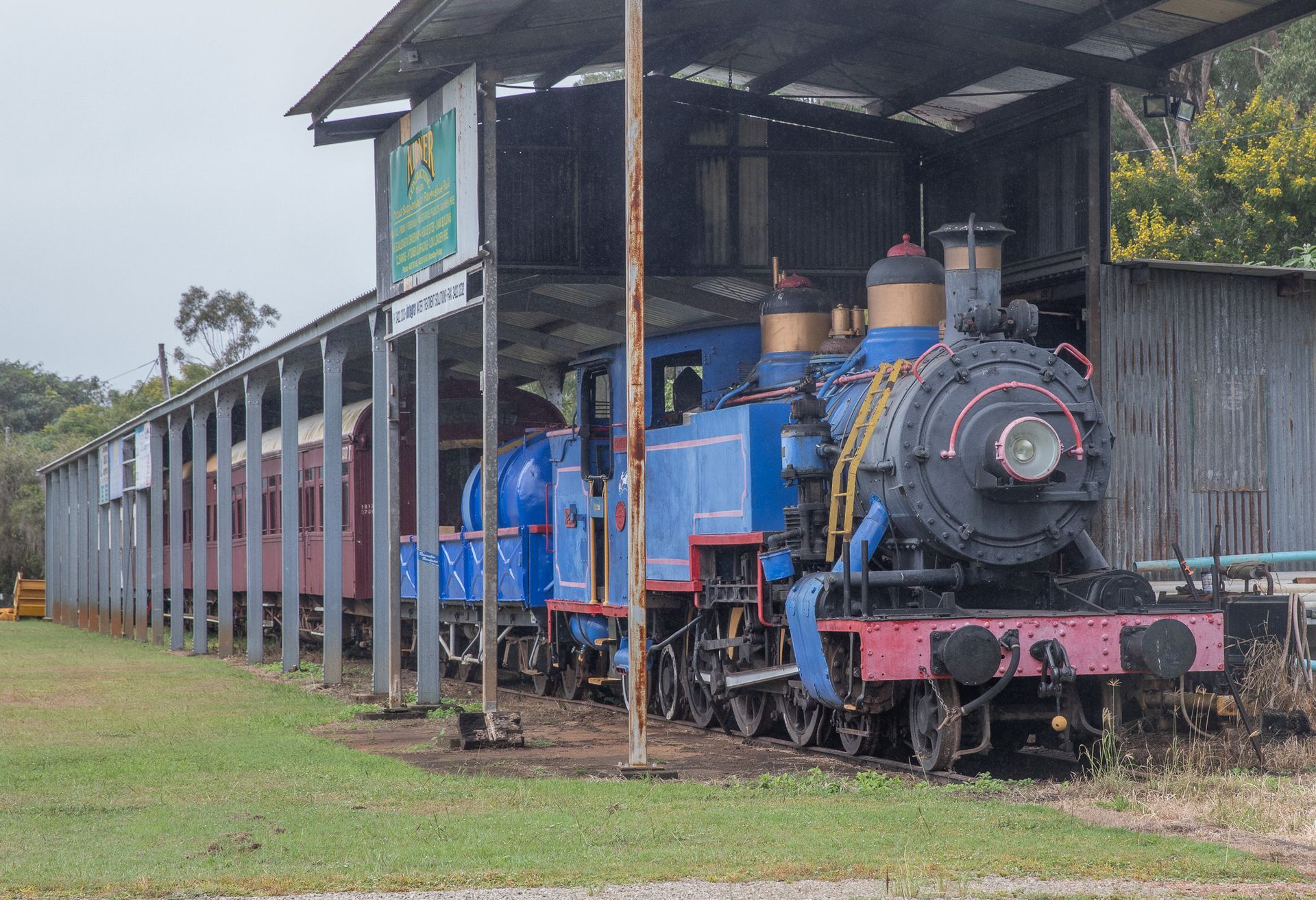 Blue steam engine and red passenger cars under a shelter.