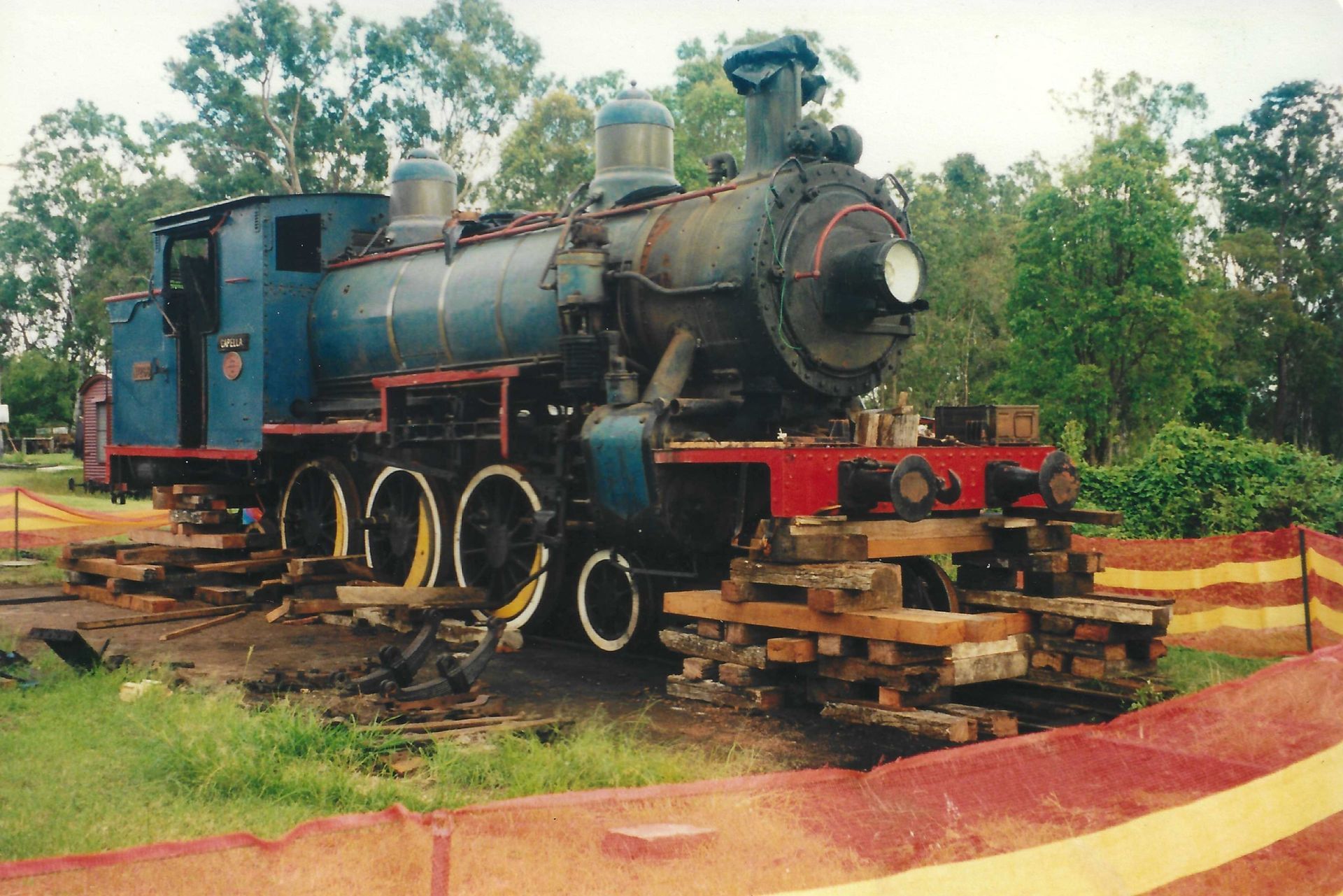 Steam locomotive, blue and black, on wooden supports, outdoors.