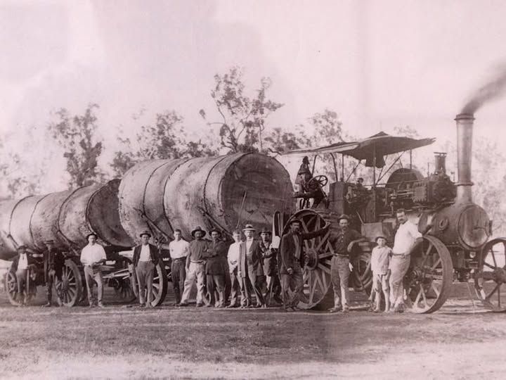 Steam-powered tractor pulling large barrels; group of men pose beside the machine in a field.
