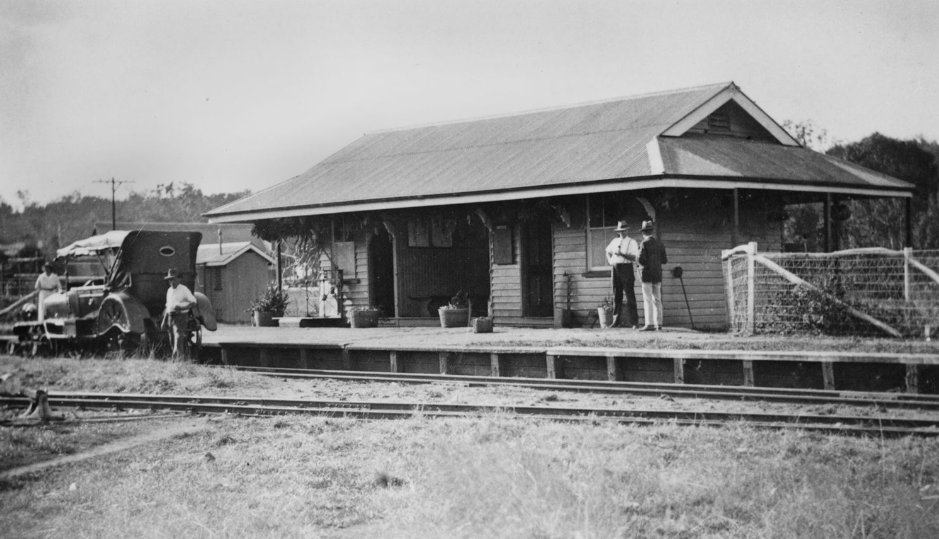 Vintage train station with people, a truck, and railway tracks.