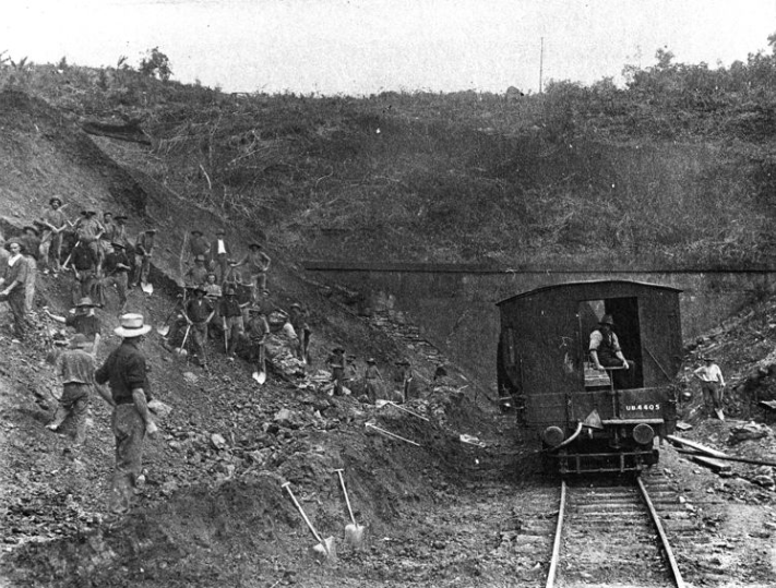 Workers and small train near a tunnel entrance; dirt and debris surround the tracks.