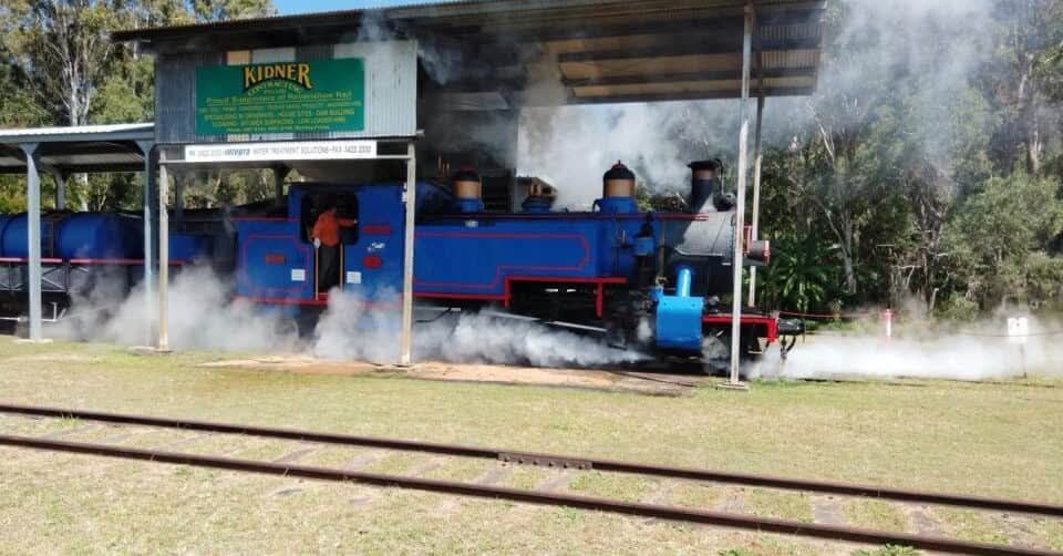 Blue steam train emitting steam at a station.