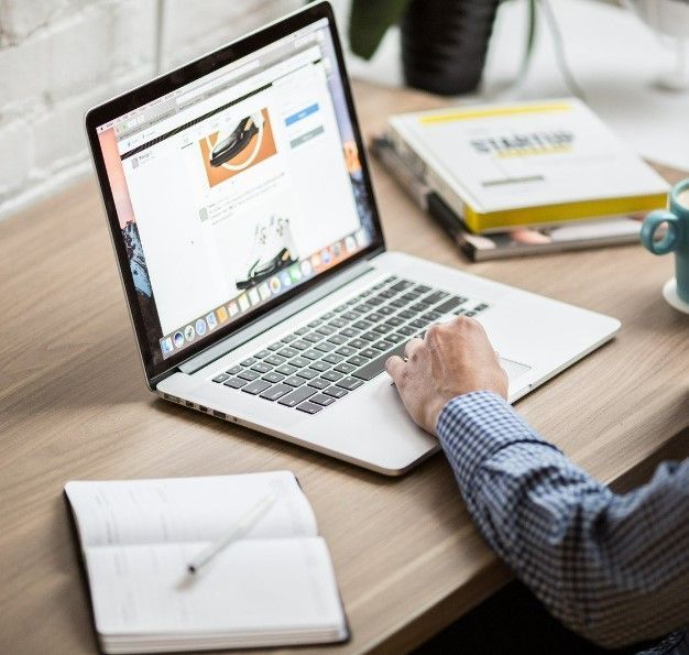A person is typing on a laptop with a book on the table
