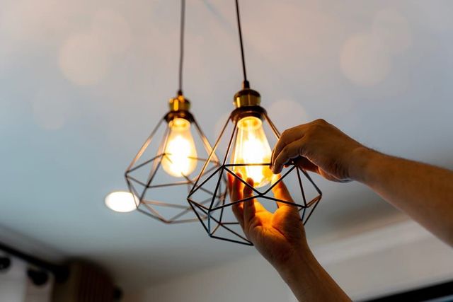 Hands adjusting two lit geometric pendant bulbs on a ceiling fixture