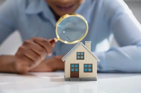 A person is looking at a model house through a magnifying glass.