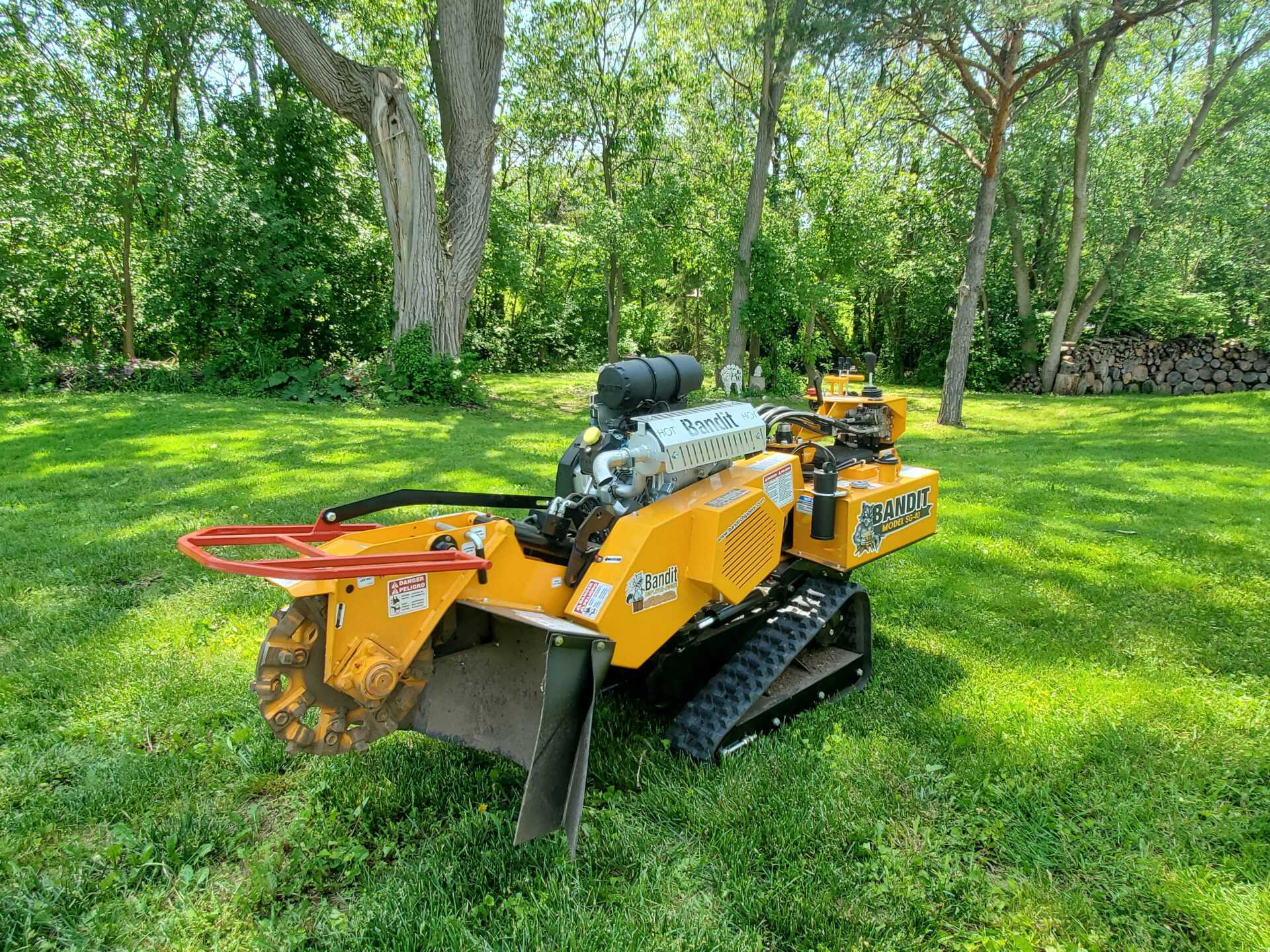 A yellow stump grinder is sitting on top of a lush green field.