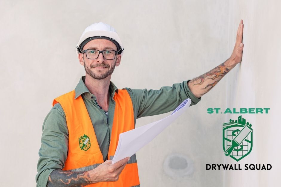 A drywall repair technician, wearing an orange safety vest, green shirt, and white hard hat, holds a commercial construction blueprint in one hand while leaning toward a wall with the other. He is inspecting work near Cranston Pl, and Allard Way, Fort Saskatchewan, AB.