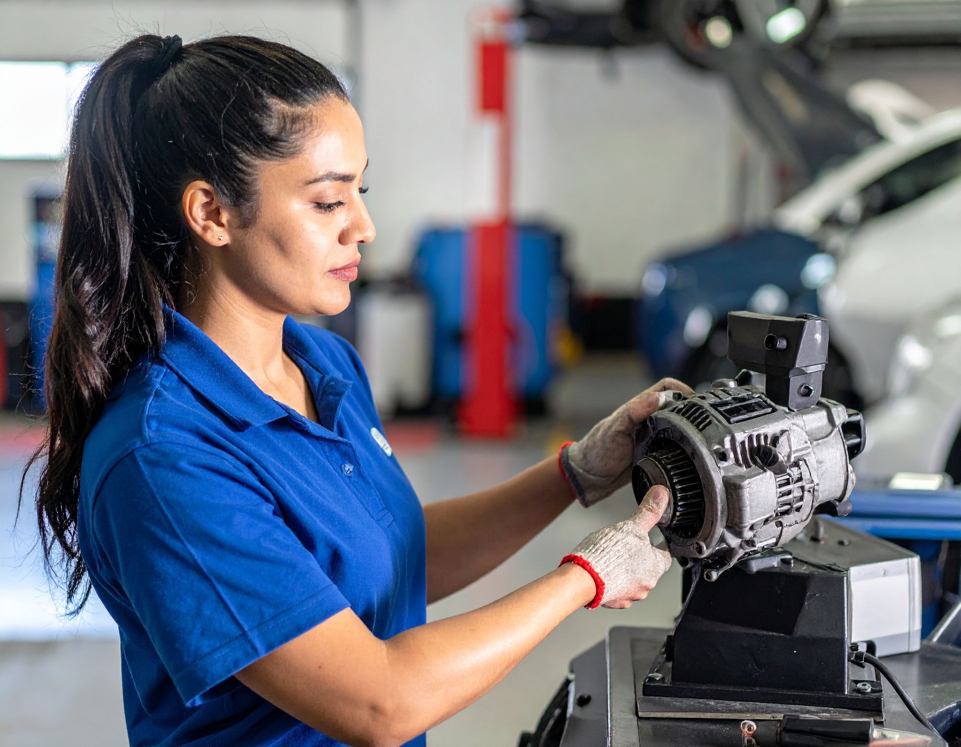 Mechanic in blue shirt and gloves working on a motor in a garage setting.