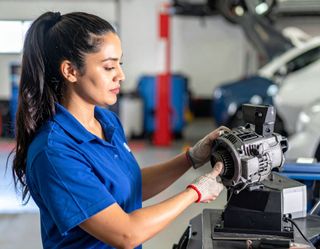 Mechanic in blue shirt and gloves working on a motor in a garage setting.