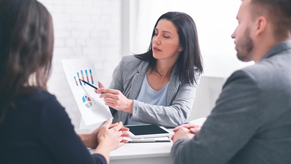 A Woman Is Giving a Presentation to A Group of People While Sitting at A Table — Twin Peaks Finance In Helensvale, QLD