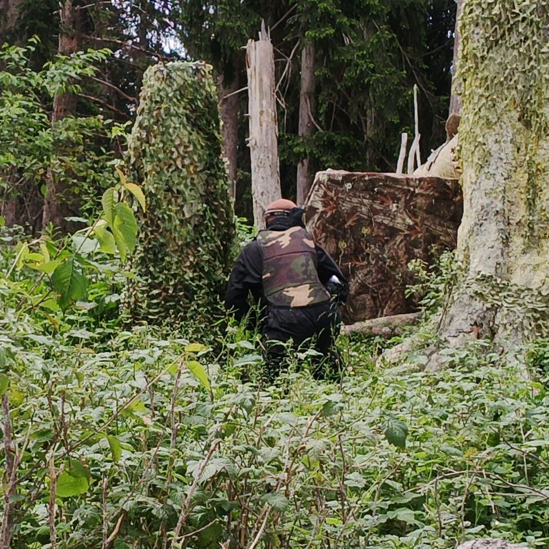 Un homme portant un gilet de camouflage se tient au milieu d'une forêt.