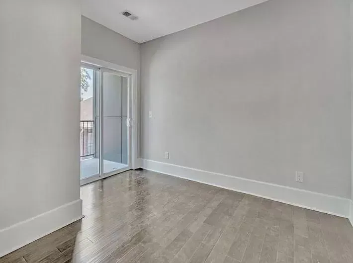 An empty room with hardwood floors and a sliding glass door leading to a balcony.