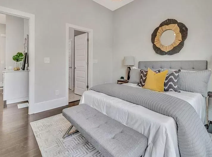 A bedroom with a bed , bench , lamp and mirror.