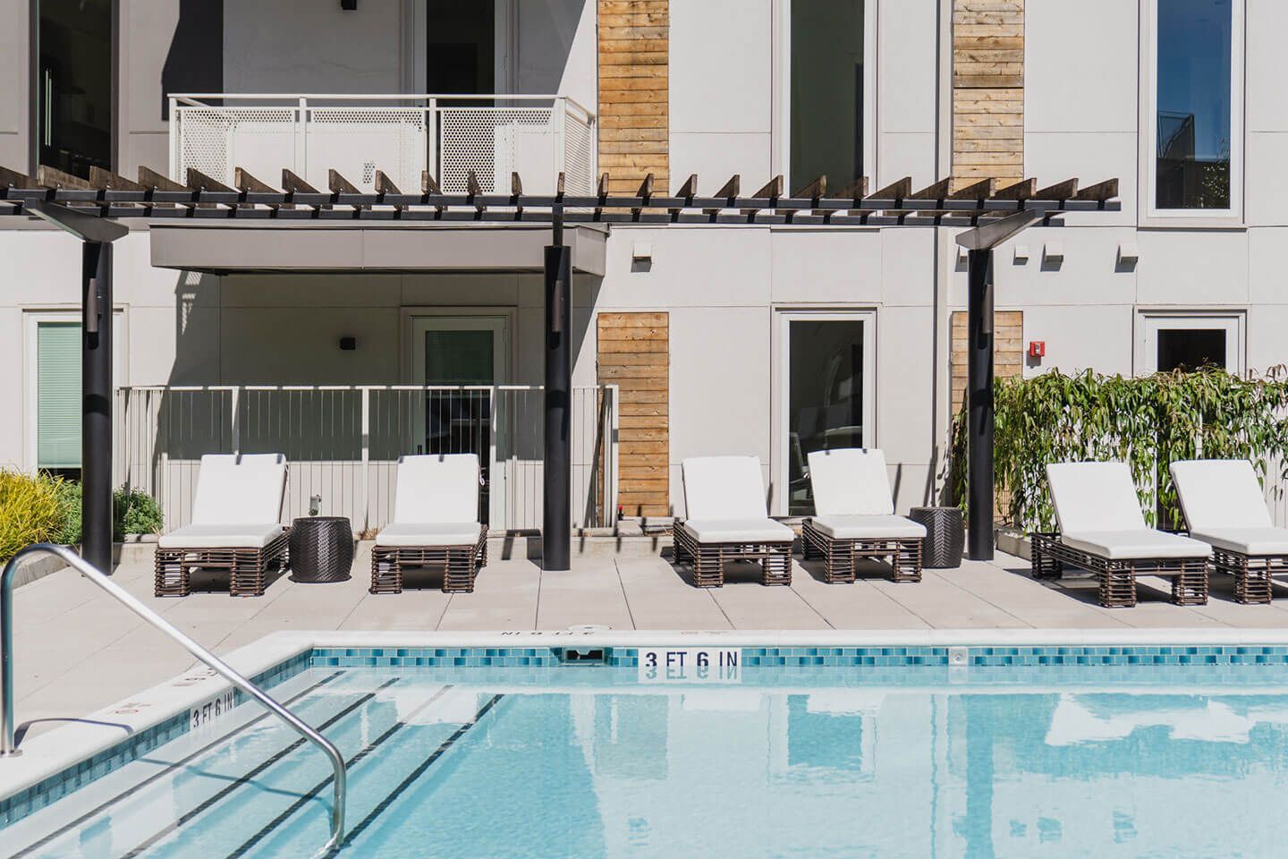 A swimming pool with chairs and a pergola in front of a building.