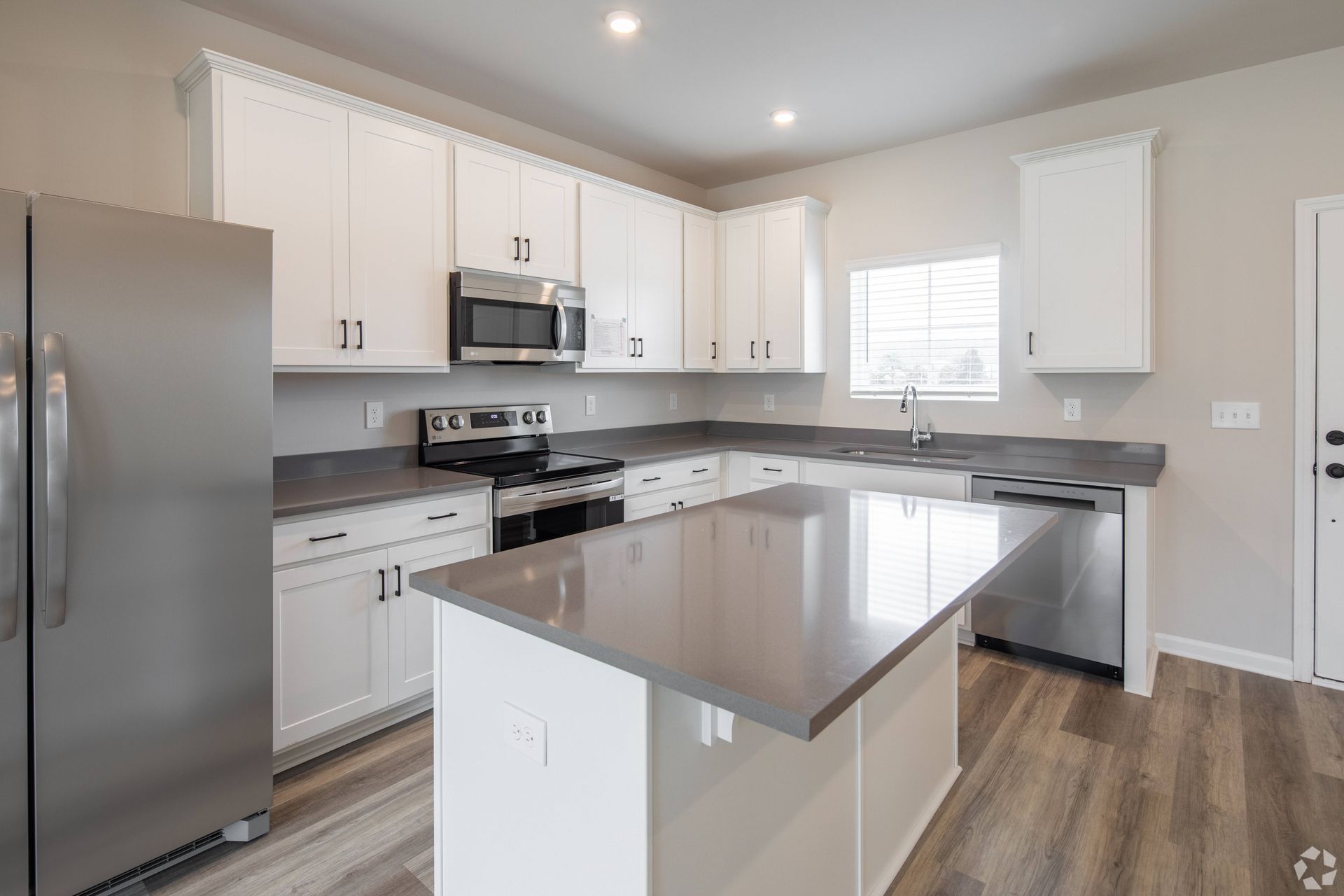 A kitchen with white cabinets , stainless steel appliances , and a large island.