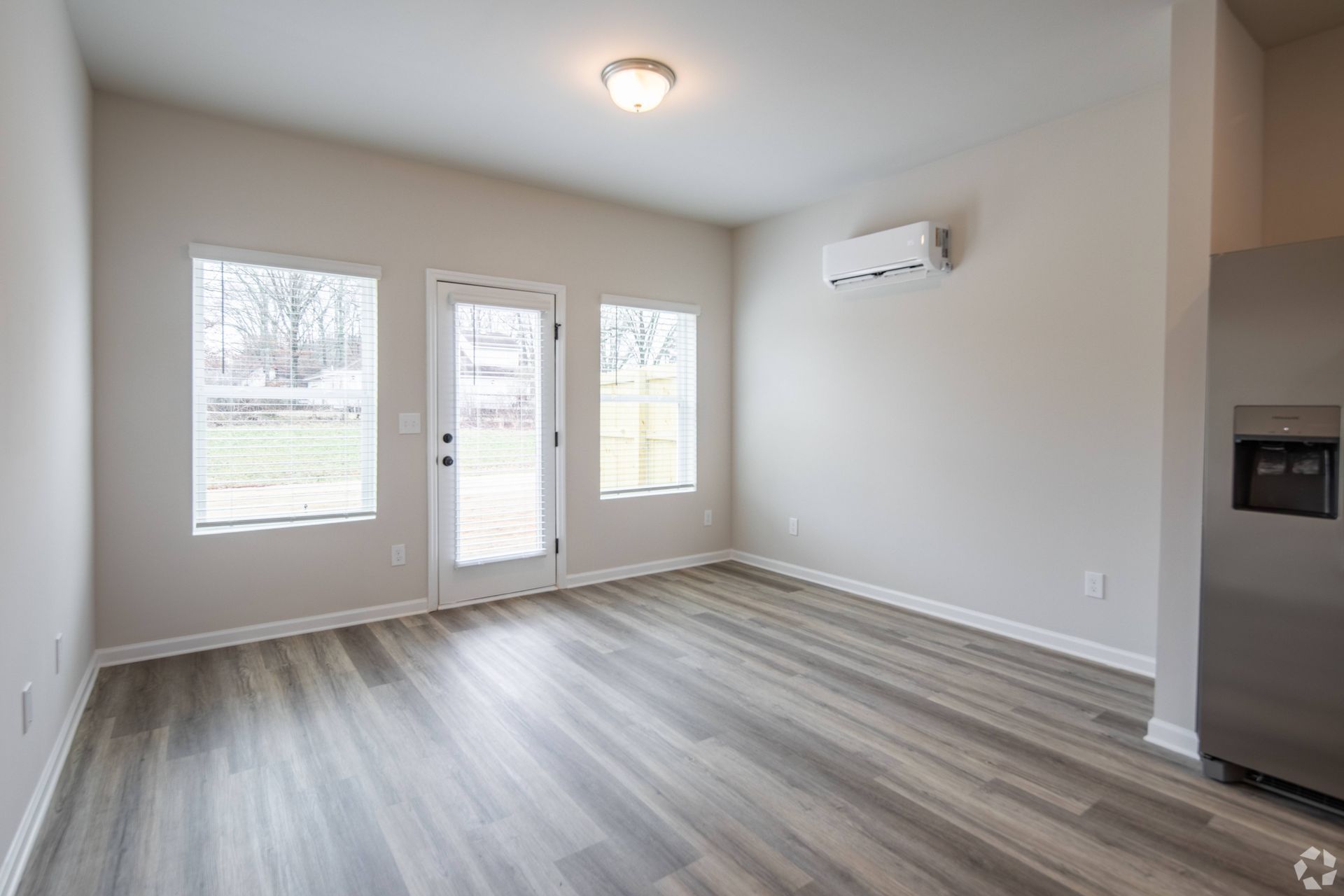 An empty living room with hardwood floors and a refrigerator.