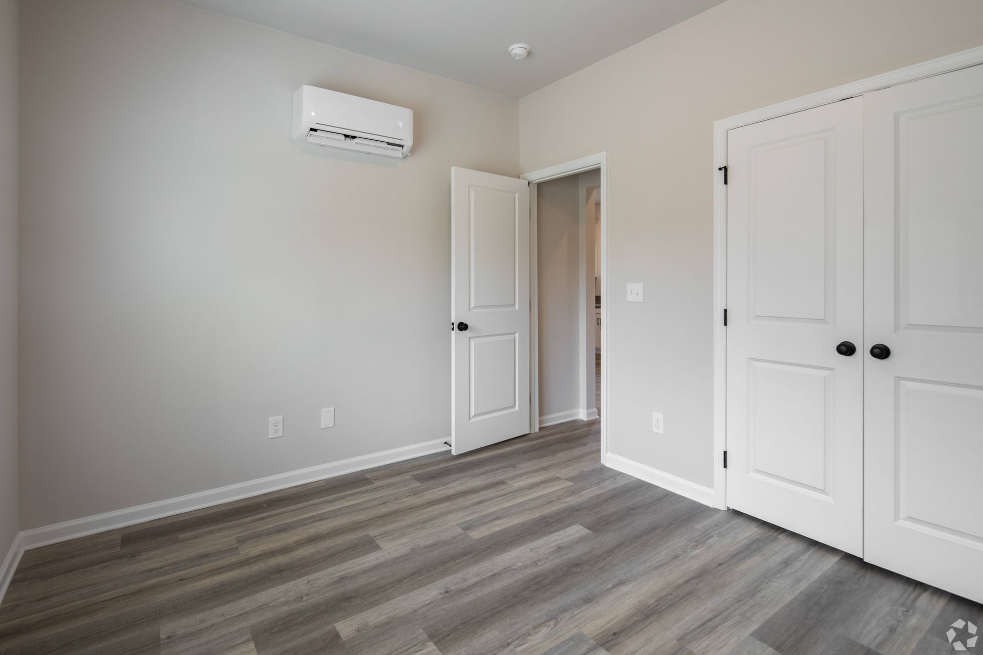 An empty bedroom with hardwood floors and white walls.