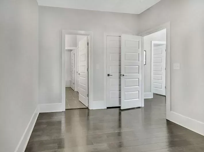 An empty hallway with hardwood floors and white doors in a house.