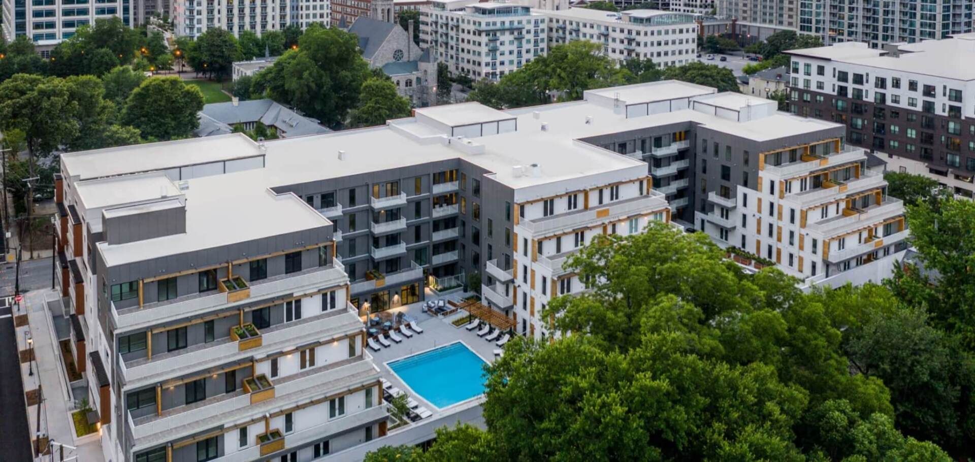 An aerial view of a large apartment building with a swimming pool surrounded by trees.