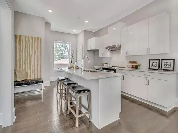 A kitchen with white cabinets and a large island with stools.