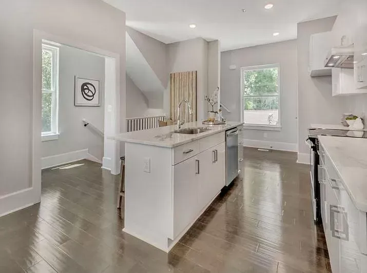 A kitchen with white cabinets , hardwood floors , and a large island.