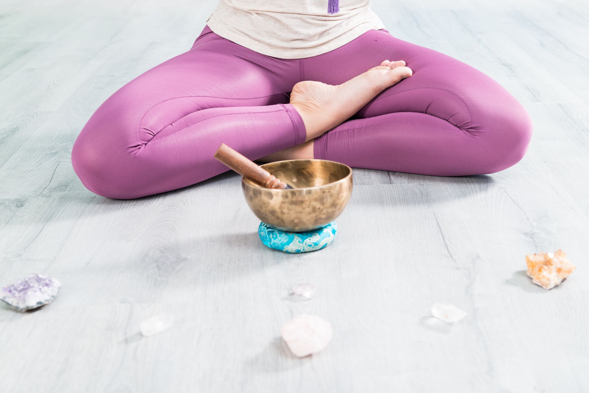 A woman is sitting in a lotus position with a singing bowl and crystals.