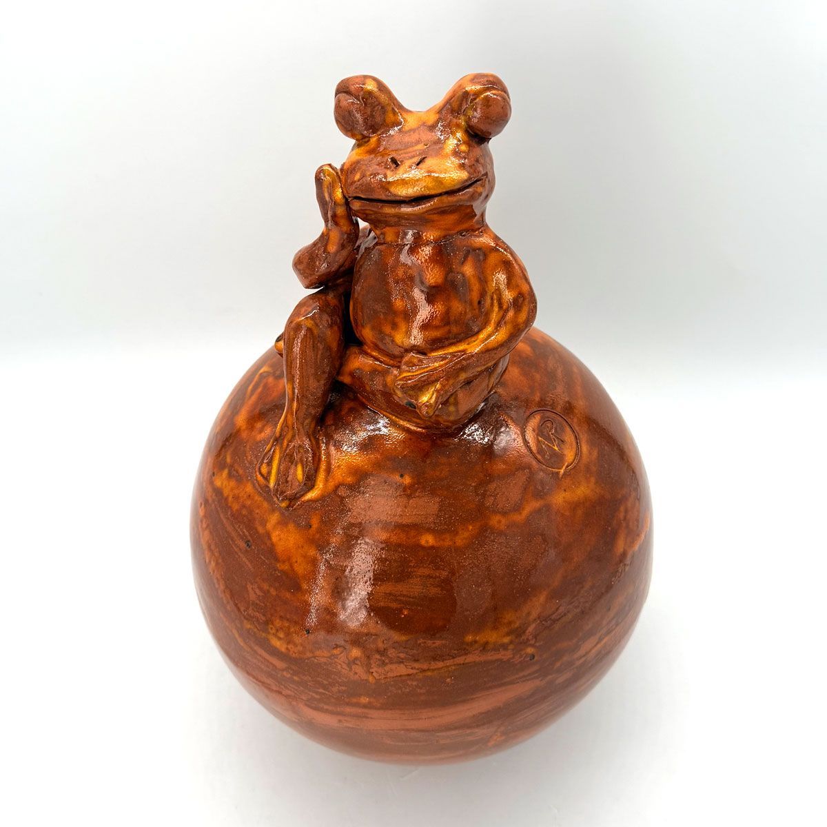 Klein bronzen kikkerfiguurtje, zittend op een ronde, gepolijste houten bol, geïsoleerd op een witte achtergrond.