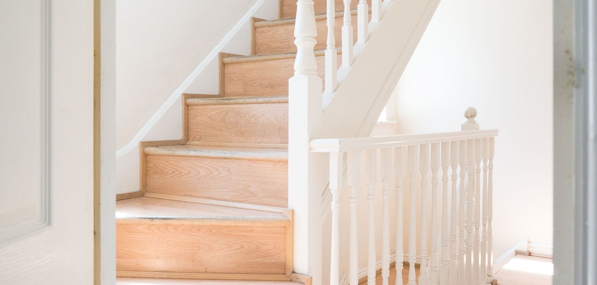 A light-colored staircase with white banisters and a railing, seen from a doorway.