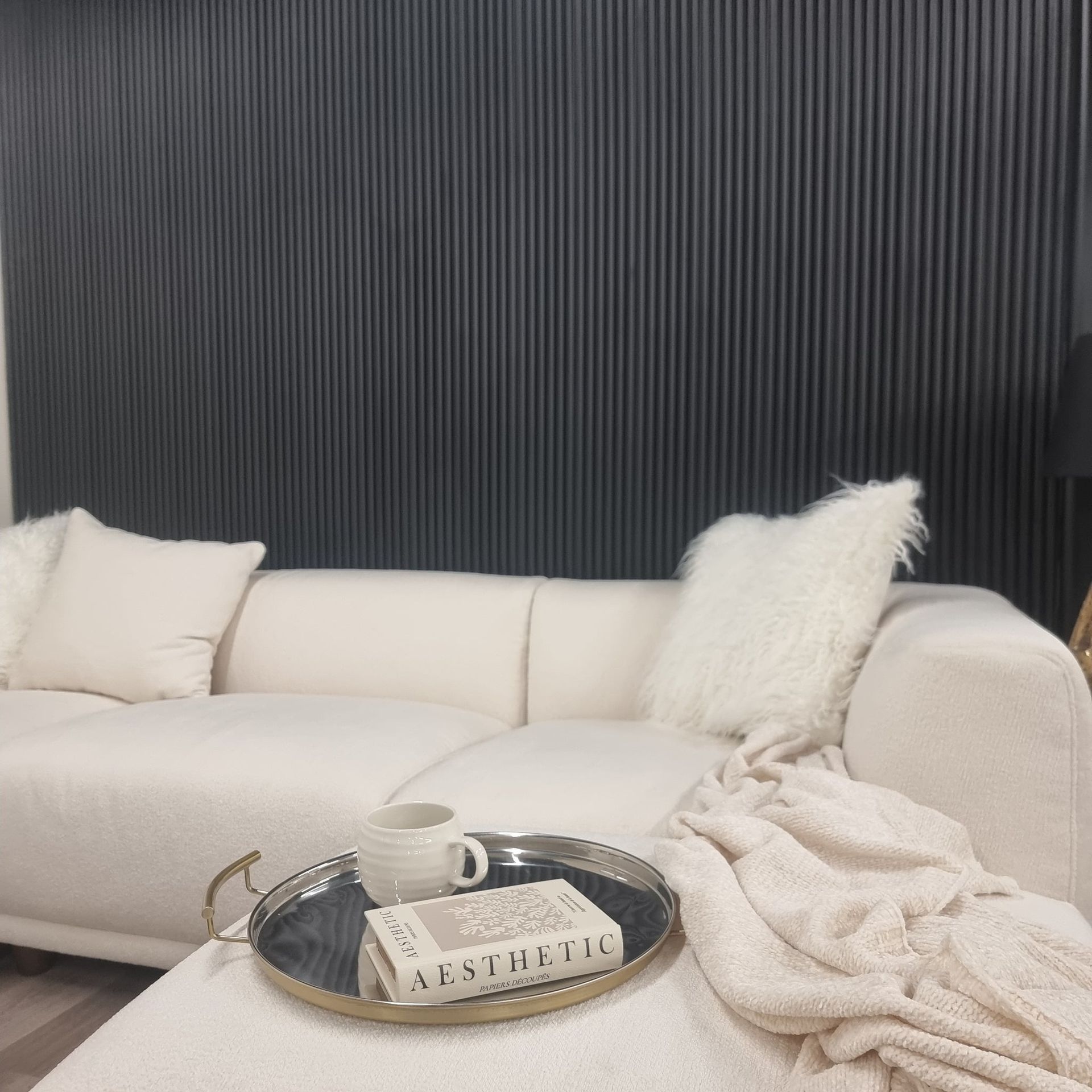 White couch with plush pillows, silver tray with mug and book, against a dark ridged wall.