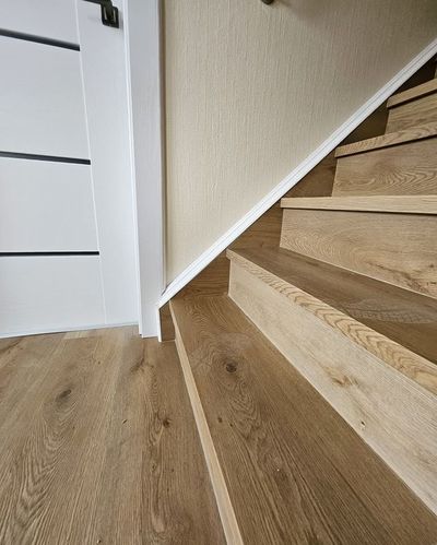 Wooden stairs with a light-colored wood floor and a white door with black accents.
