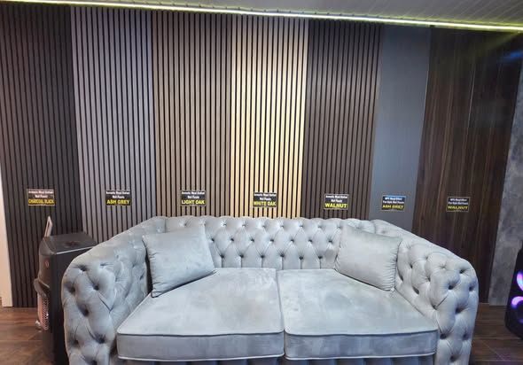 A gray tufted sofa in front of a wall with vertical wood panel samples of various brown shades.