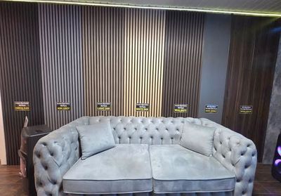 A gray tufted sofa in front of a wall with vertical wood panel samples of various brown shades.