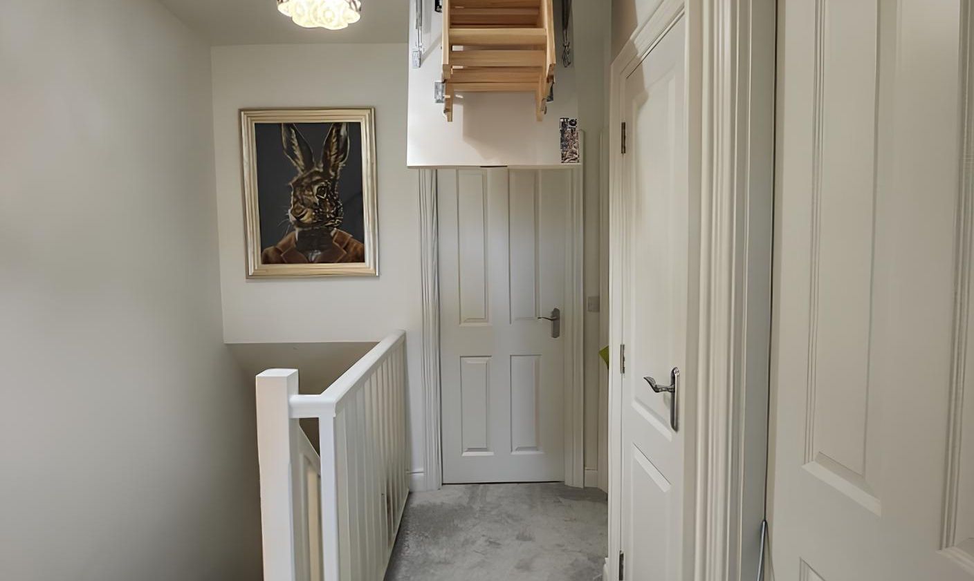 Hallway with white walls, doors, and a staircase. Painting of a rabbit hangs on the wall.