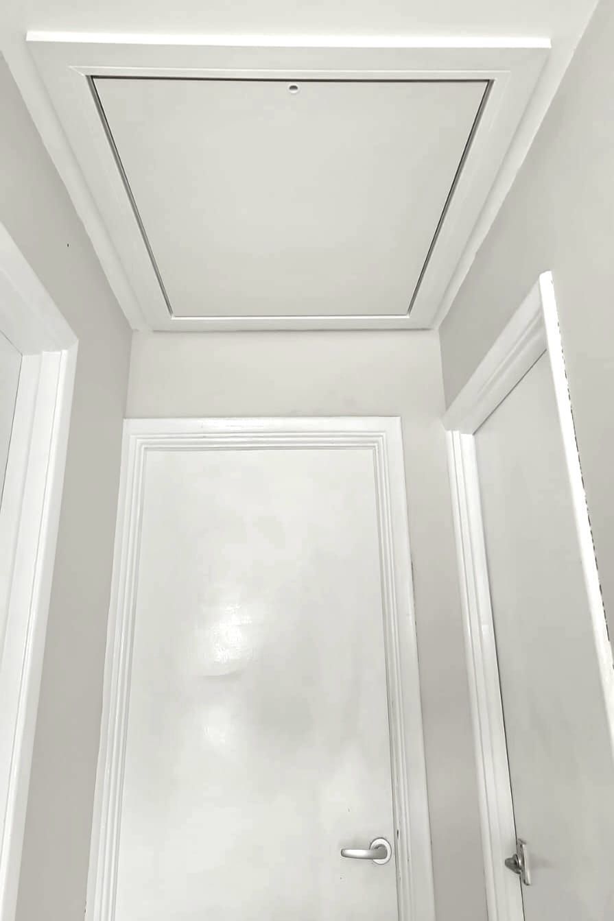 White hallway with door, overhead attic access panel.