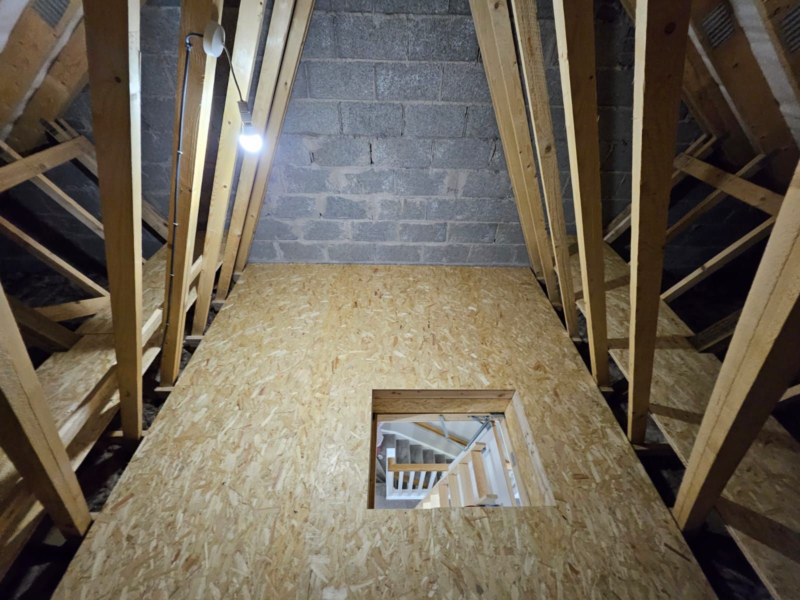 Interior of an attic: wood framing, OSB paneling, rectangular window, concrete block wall at the apex.