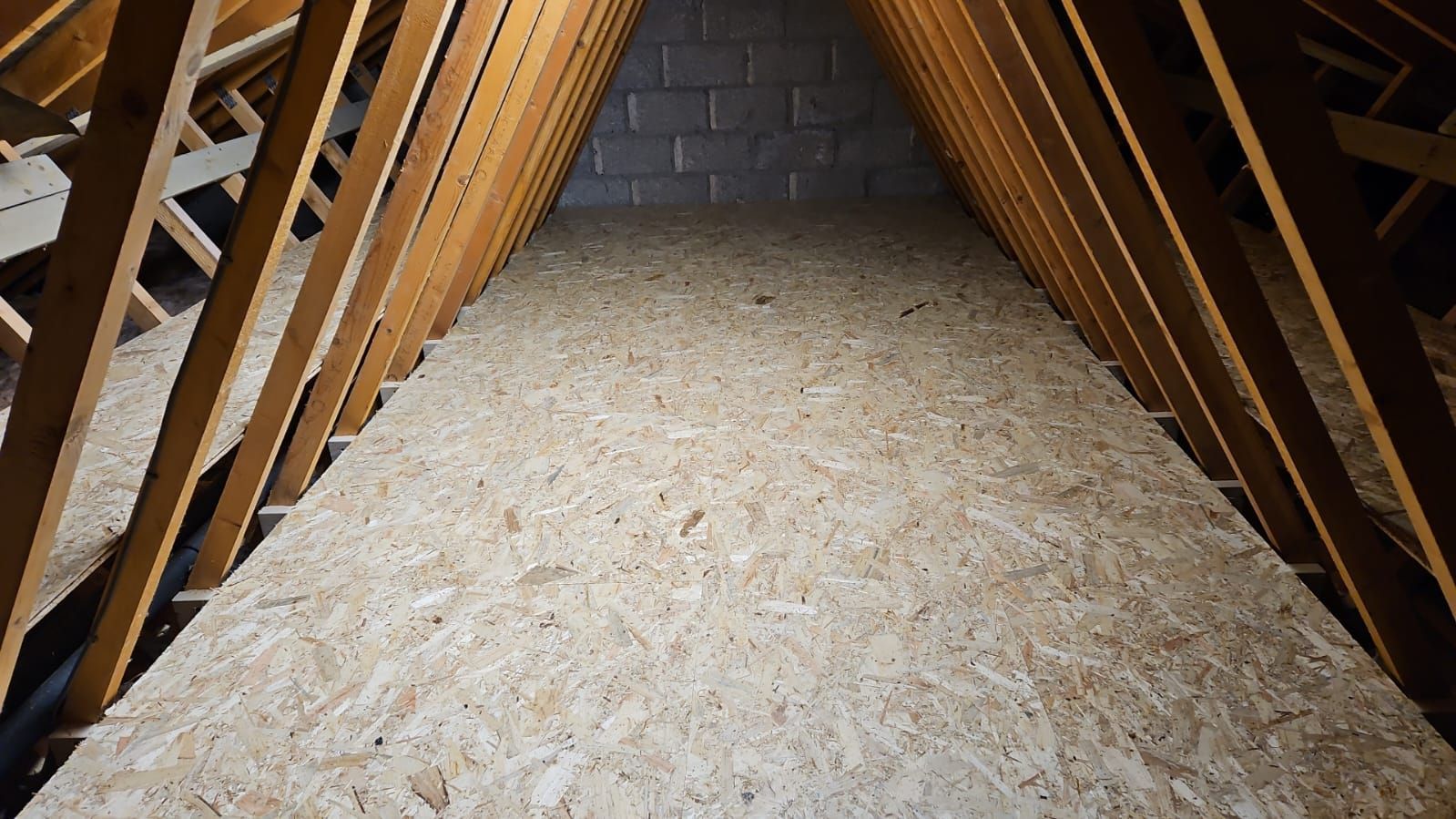 Interior view of an attic space with wooden beams and plywood flooring.