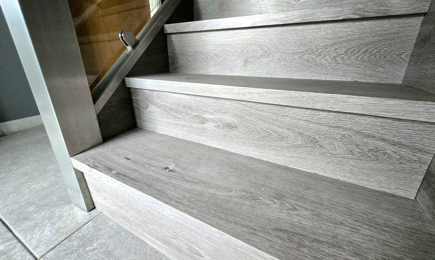 Wooden staircase with light gray treads and risers, stainless steel railing and support post.
