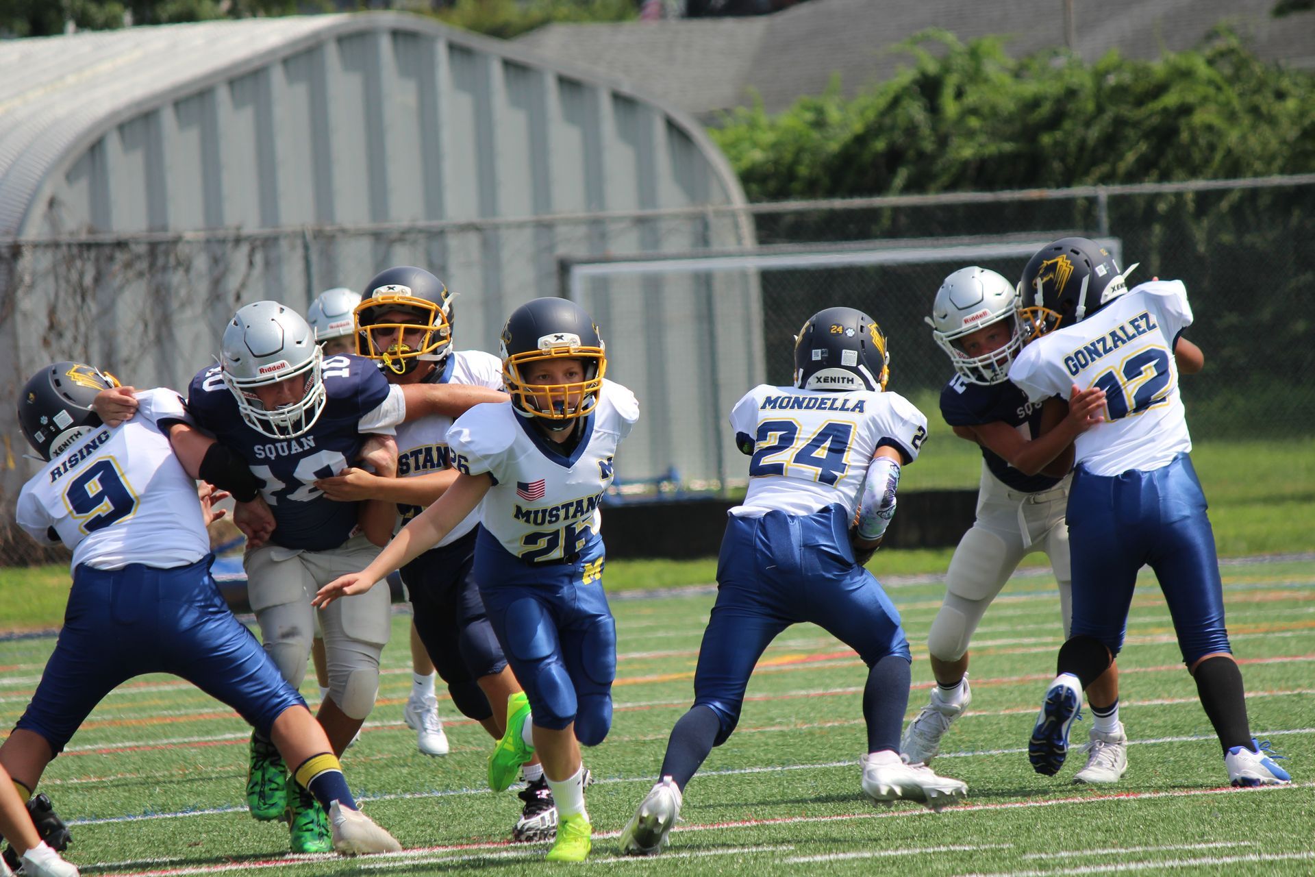 Football player in silver uniform runs with ball on a green field.