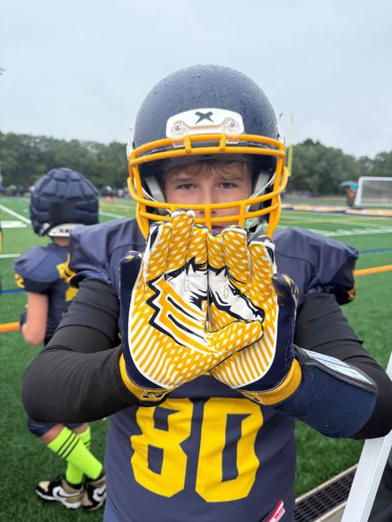 Football players in action on a grassy field; one runs with the ball, pursued by two opponents.