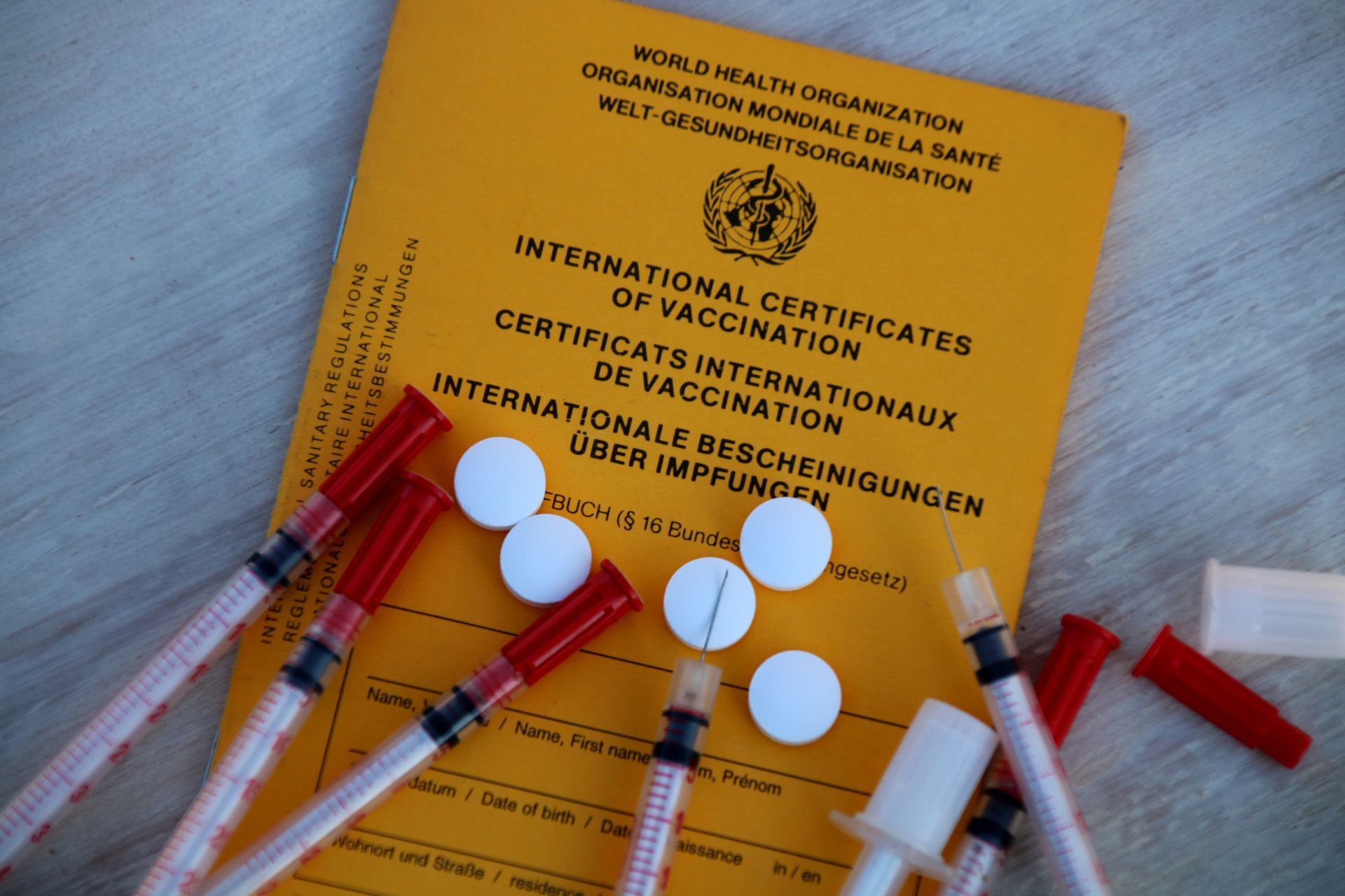 Gelber Impfpass mit Spritzen und Tabletten.