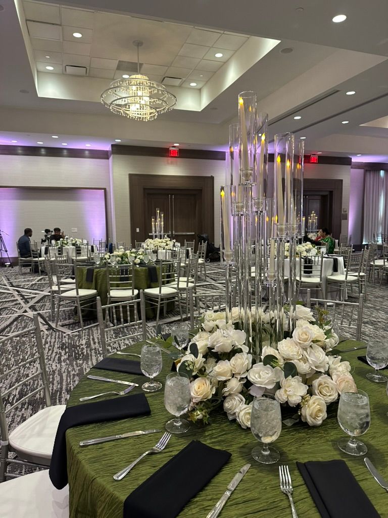A banquet hall set for a wedding reception with round tables featuring green tablecloths, floral centerpieces, and glass.