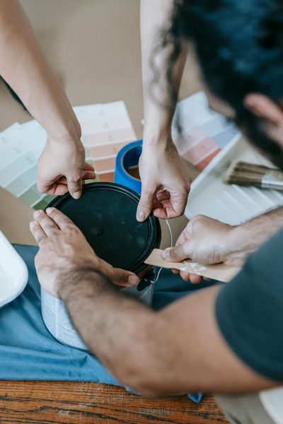 People opening a paint can together, paint swatches, and brushes on a table.