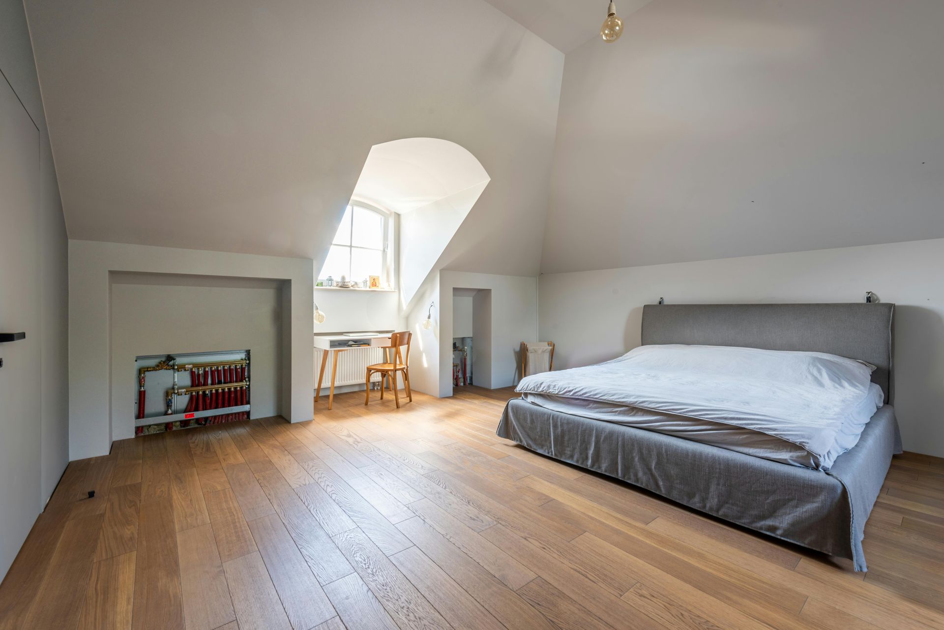 Bedroom with sloped ceiling, hardwood floors, bed, desk near window, and built-in shelving.